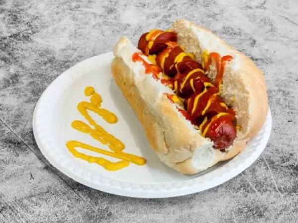 A loaded American beef hot dog in a soft bun, topped with ketchup and mustard, on a plate.