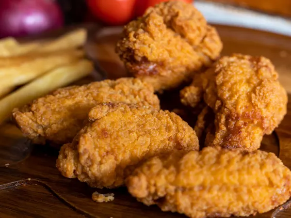 Golden, crispy Southern-fried spicy chicken wings served on a wooden board with fries.